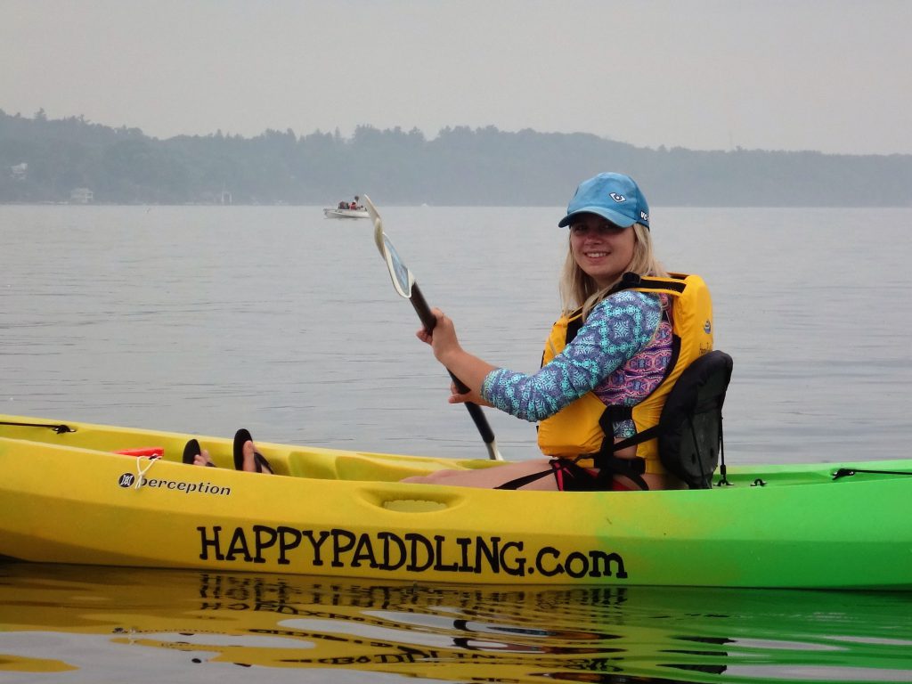 Blond girl wearing a blue shirt and hat in a yellow kayak