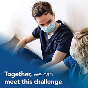 Together, we can meet this challenge. Two nursing students sitting against a wall wearing masks