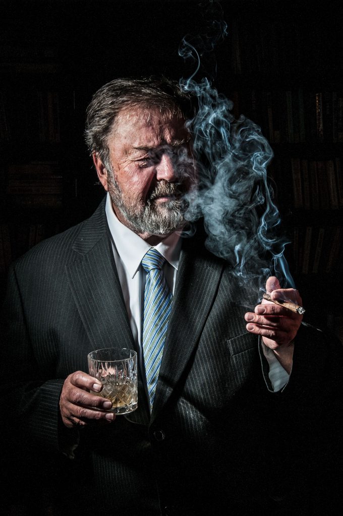 Man with beard in suit drinking whisky and smoking a cigar