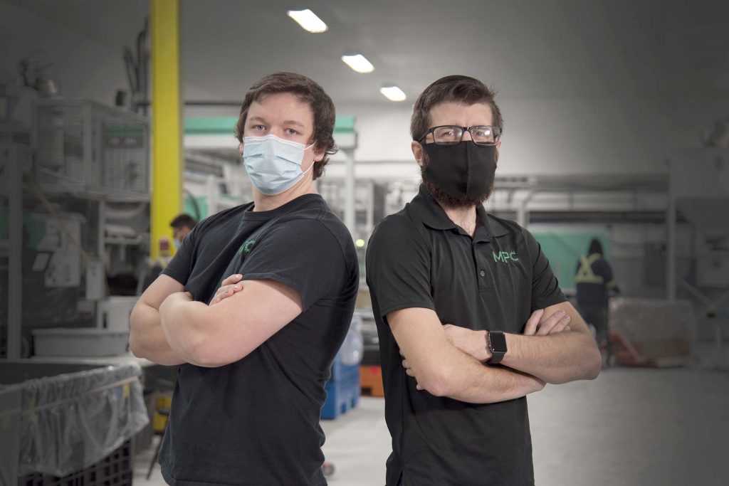 Alumni Justin Johnson and Kyle Morton stand back to back in a manufacturing plant