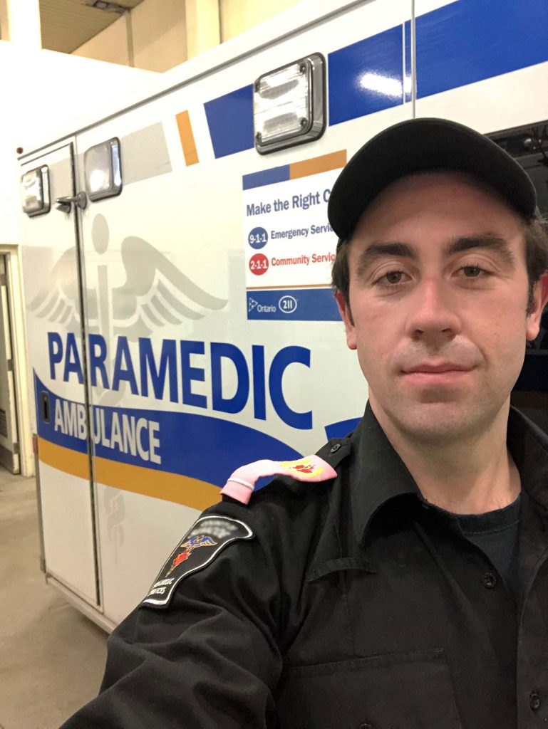 Paramedic alumnus Shane Ellis stands in front of his ambulance, in uniform