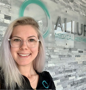 Alysha van Gaalen - grad of School Within a College, headshot of young woman wearing glasses with medium-length blonde hair, standing in workplace at medical aesthetics centre