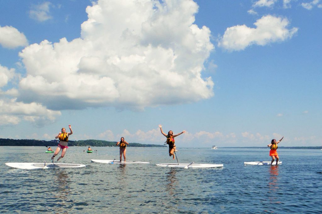 Four women jumping off stand up paddle boards in Lake Simcoe in Barrie, Ontario