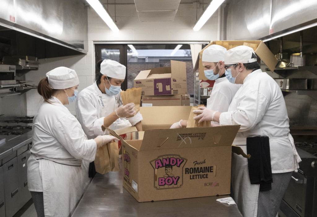 Four people wearing white chef unifors loading up boxes in a kitchen