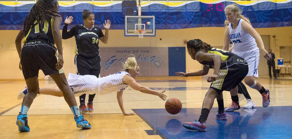 Five women playing basketball, one player diving for the ball