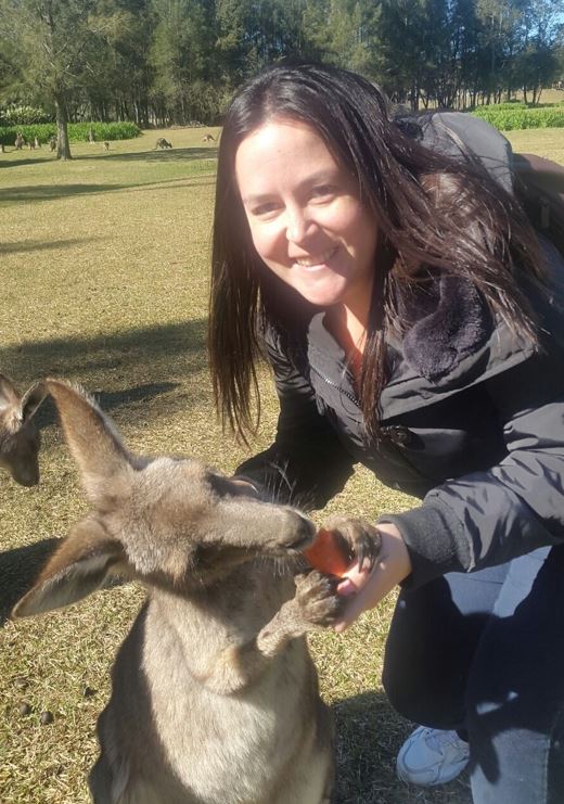 A person smiles next to a kangaroo that's eating out of their hand.