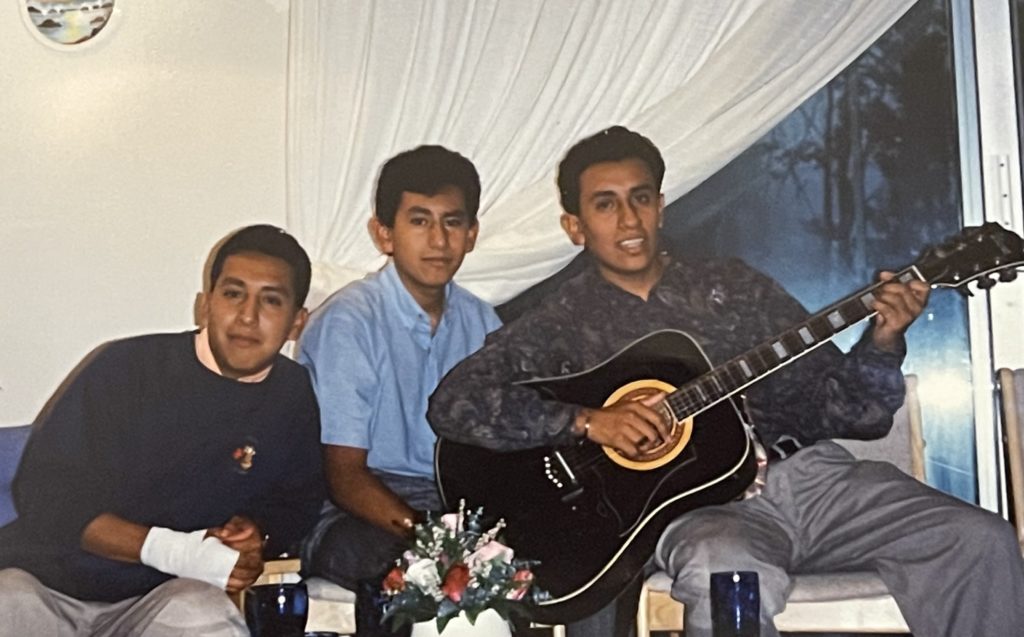 Three adults sit together and smile for the photo, while one of them holds a guitar.