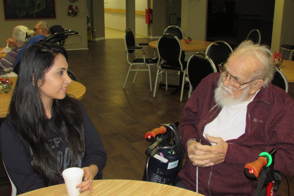 A young woman has coffee with an elderly gentleman at a seniors' home