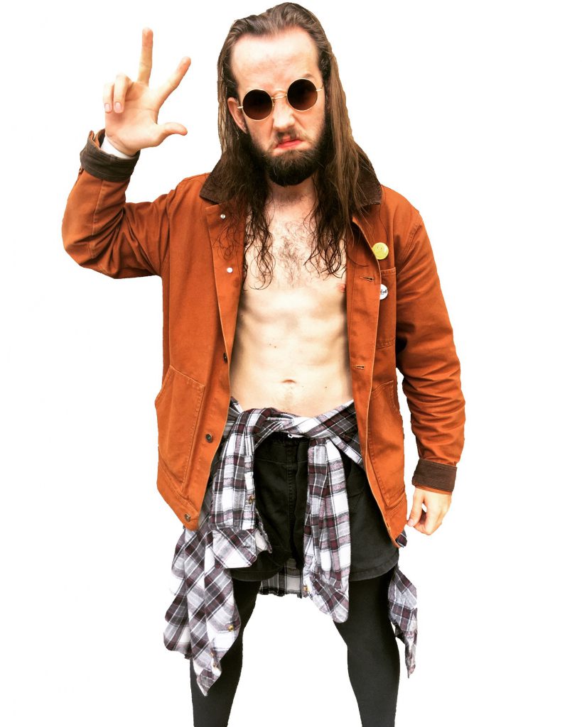 A person with long brown hair and beard, and who's shirtless, with circular sunglasses, an undone orange jacket, black tights, black shorts, and a plaid shirt tied around their waist, grimaces and holds three fingers up on one hand.