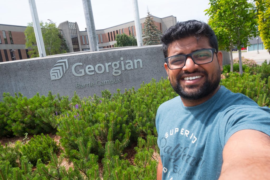 A man takes a selfie in front of a Georgian College sign at the Barrie Campus of the college