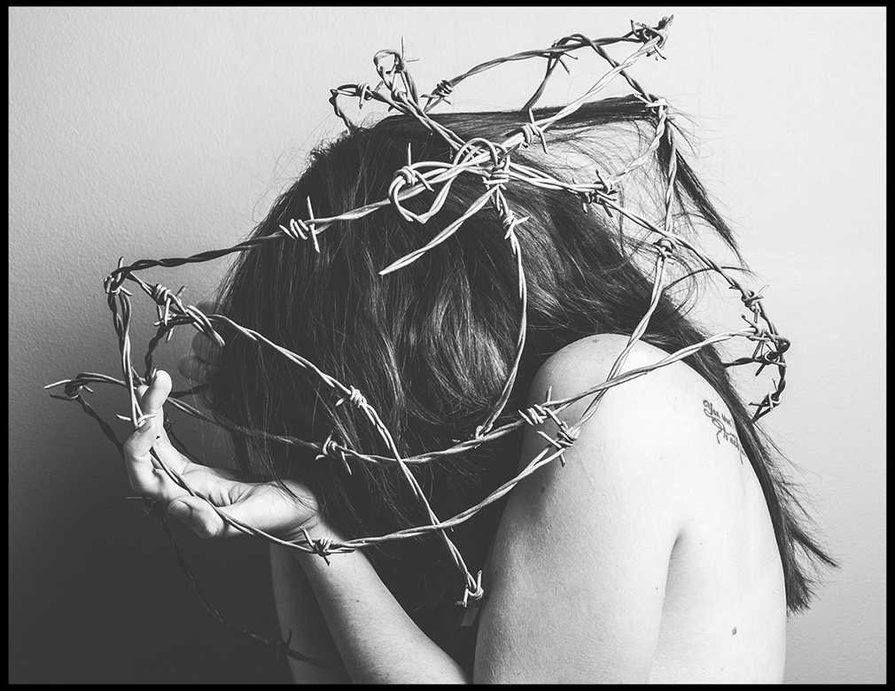 Black and white photo of a girl with her head down covered in barbed wire