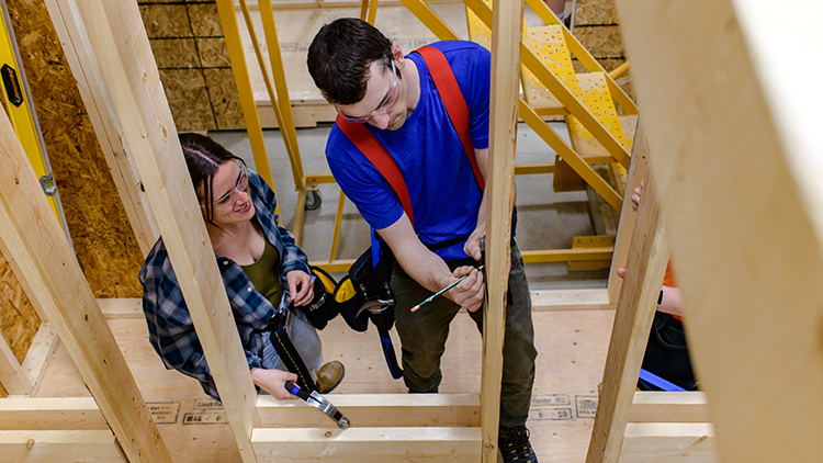 Female-and-male-construction-trades-pre-apprenticeship-students-measure-out-a-board-of-a-home-trainer-in-the-shop-space