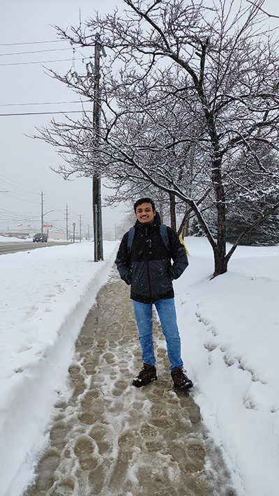 Hemchandran wearing a winter coat and backpack, on a snow barrie sidewalk