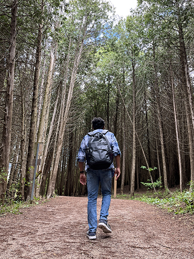Hemchandra hikin through a Canadian forest, wearing a backpack