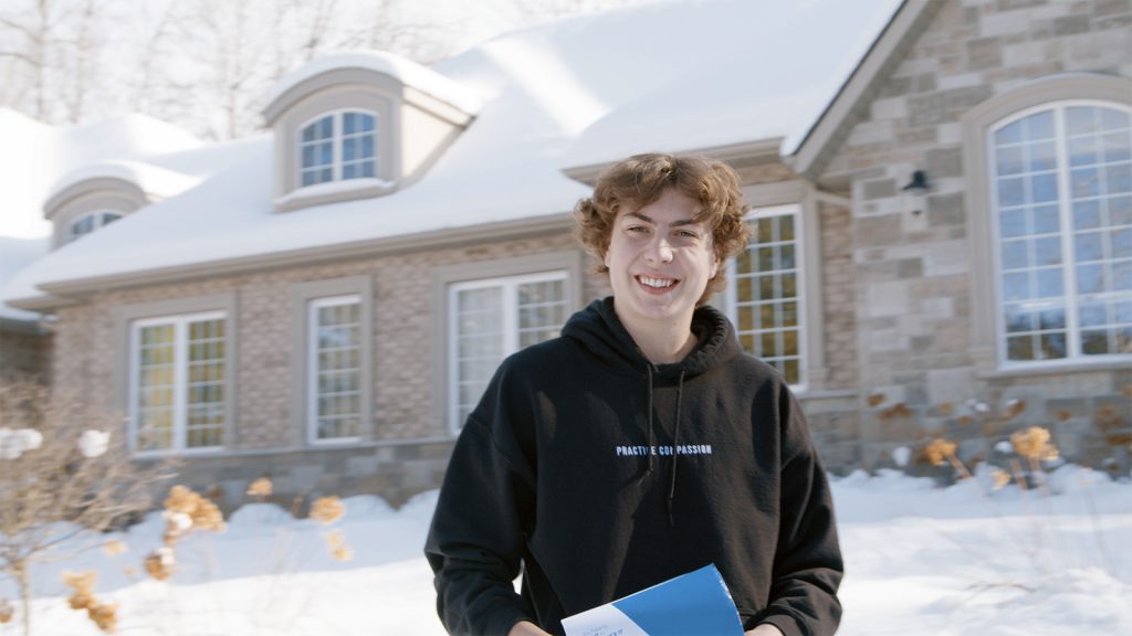 A young male standing outside his houe with a package