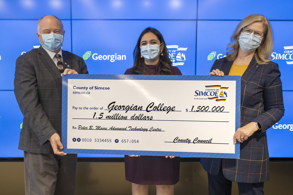 Three people (a male and two females) holding a big cheque for $1.5 million. They're standing in front of a blue screen.