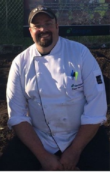A smiling man in a white chef's coat.
