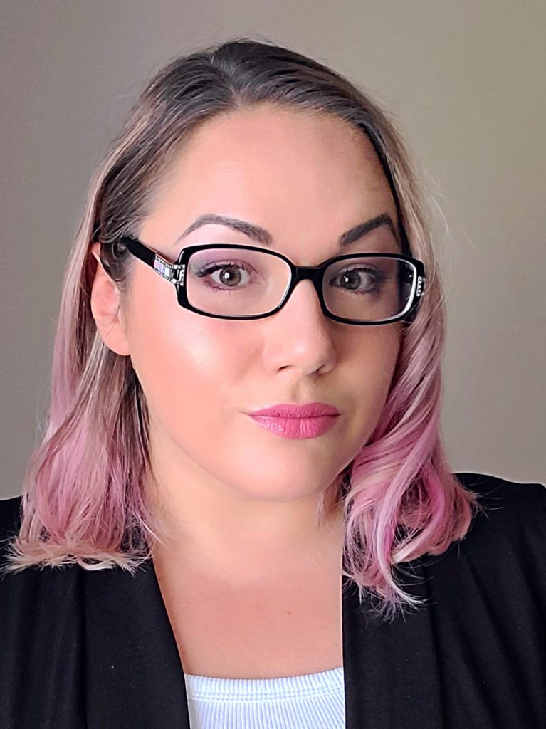A head shot of a female with pink hair and glasses