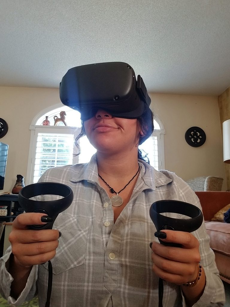 A woman wearing black goggles and holding two control switches in her hands. She's standing in a livingroom.