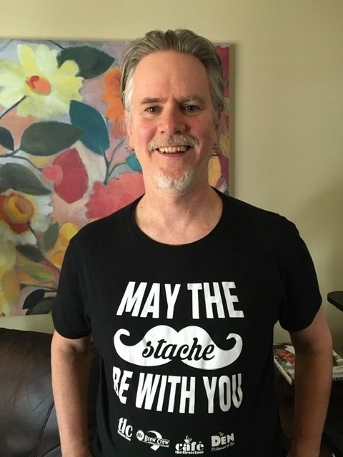 Person smiles at the camera while wearing a shirt that reads "May the stache be with you."