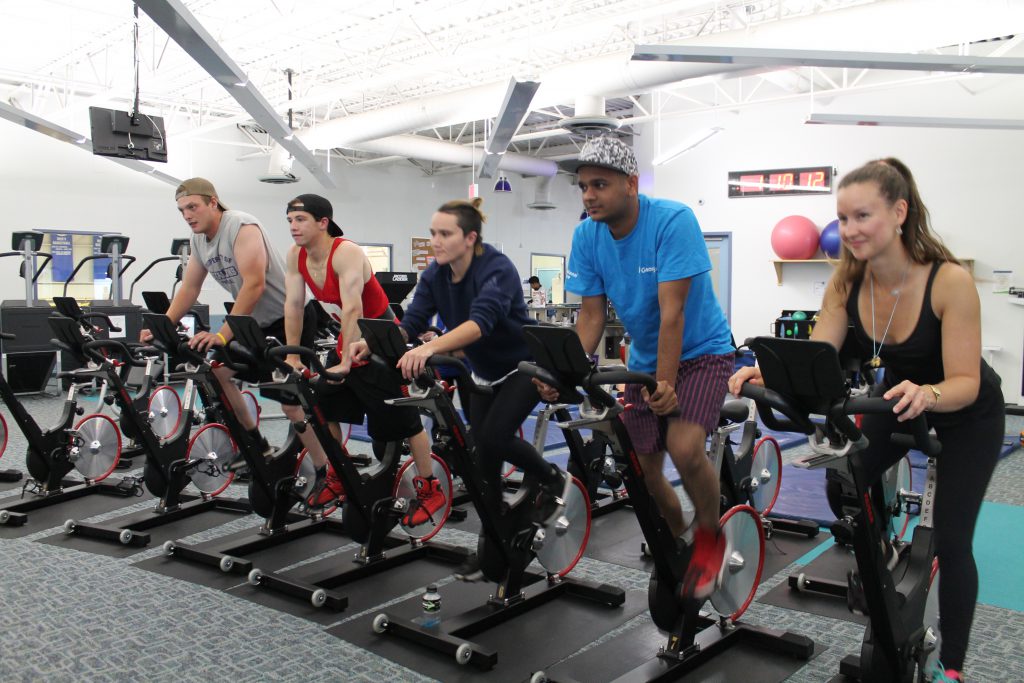 a group of female and male students in the fitness centre exercising on stationary bikes