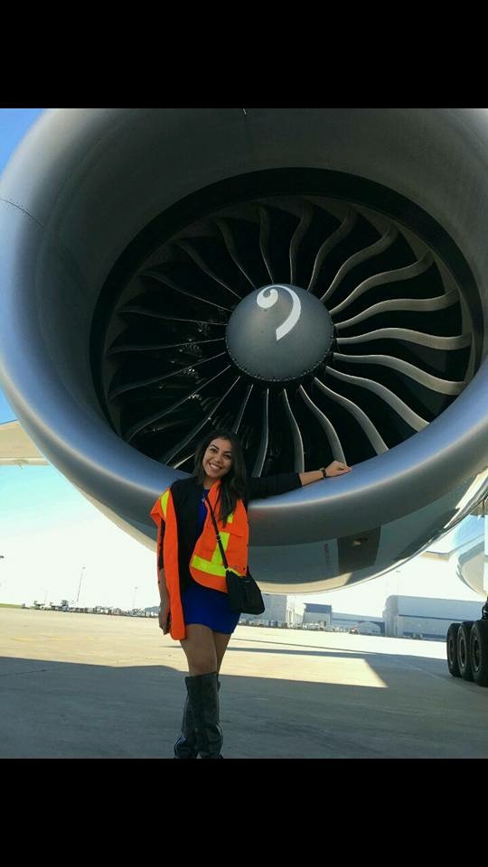 A woman wearing a safety vest stands in front of an airplane