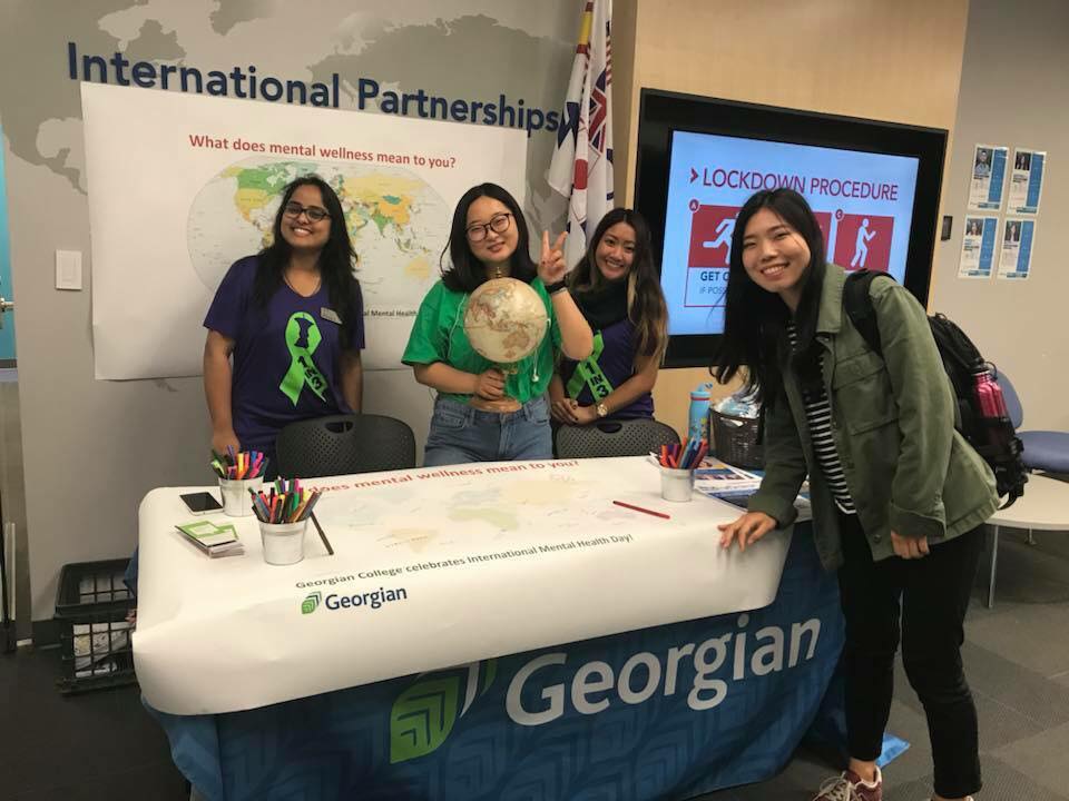 Four young women standing at a booth to welcome students to the international centre at Georgian