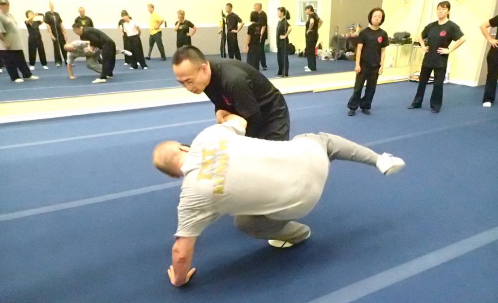 Two people grapple in martial arts, while other people stand around them.