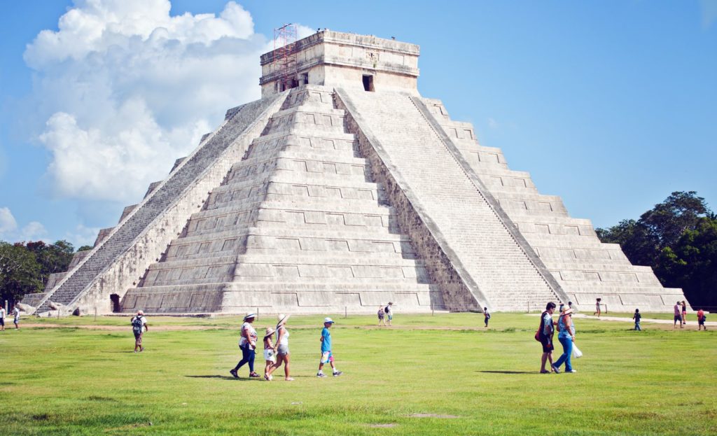 Chichen Itza in Mexico - a pyramid structure with steps on each side to the top. People walk in the grassy foreground.