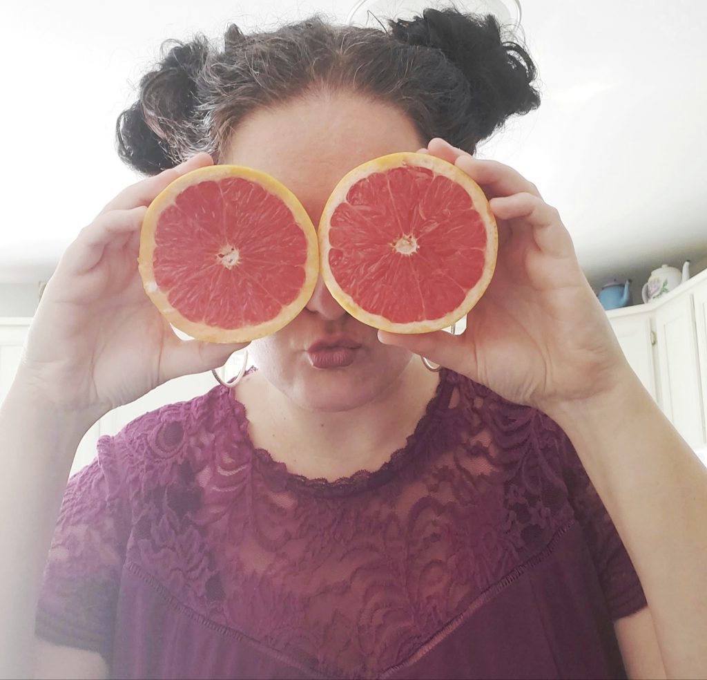 Person holds up cut grapefruit halves in front of their eyes.