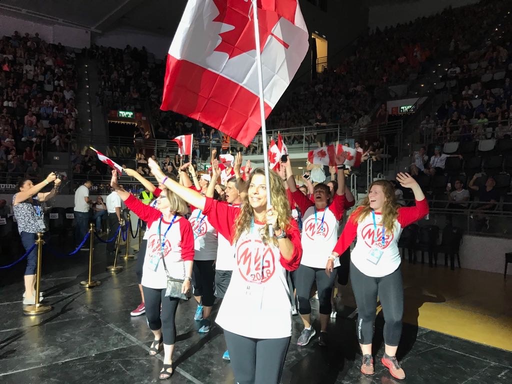 Group of people wave, with the person in front carrying a Canada flag.