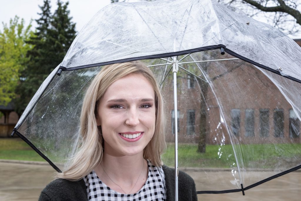 Blonde female Georgian College co-op student smiling with an umbrella in the rain.