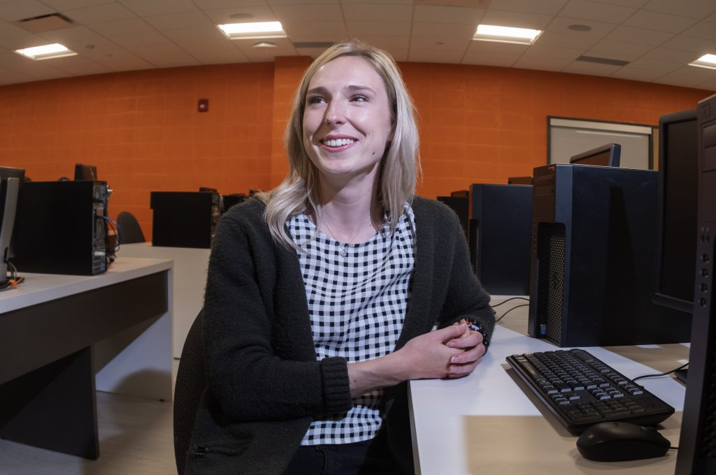 Female Ontario College co-op student in a computer lab with an orange background.