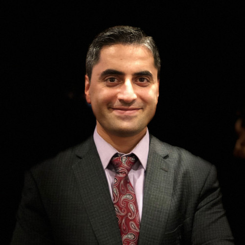 Majid wearing a grey suite with a black background
