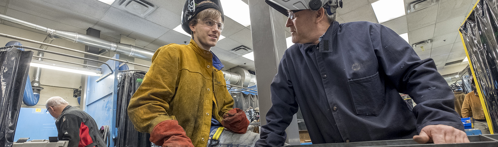 Welding instructor works with a student on a project in the shop space