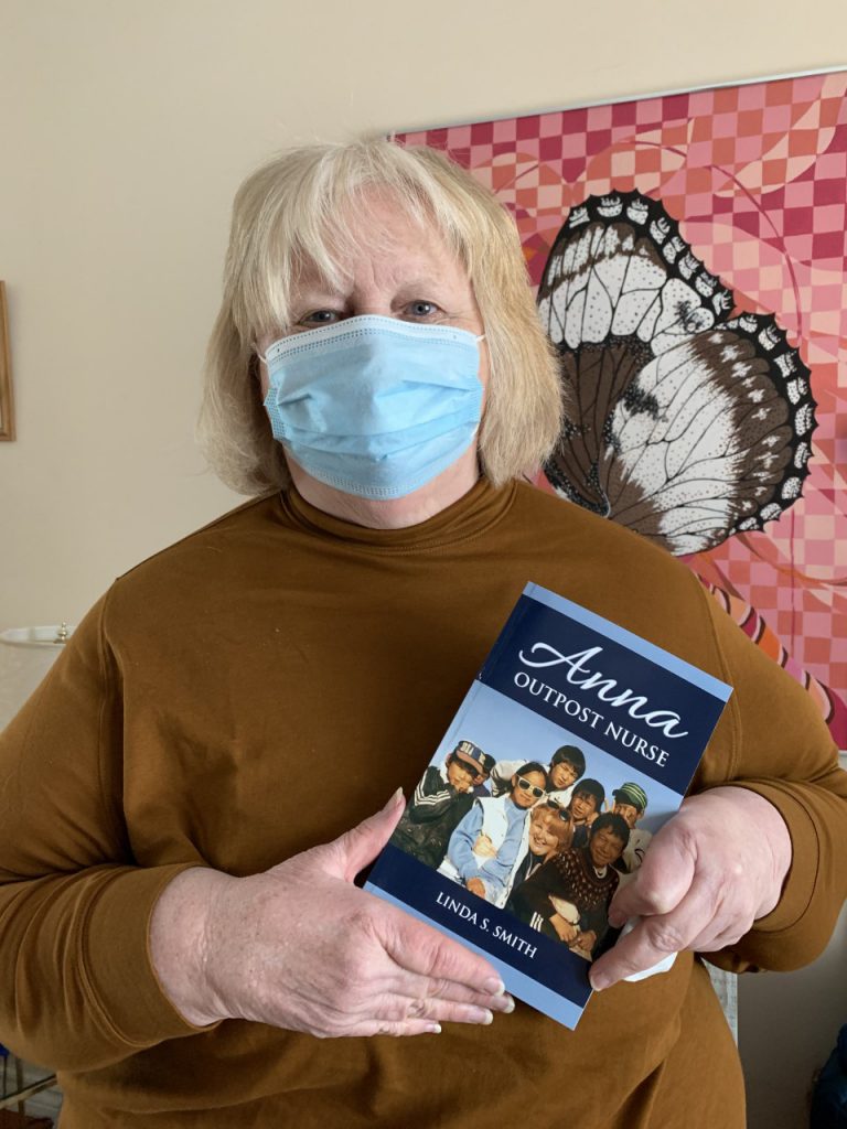 Retired nurse Anne Moller holding a printed copy of her book: Anna: Outpost nurse