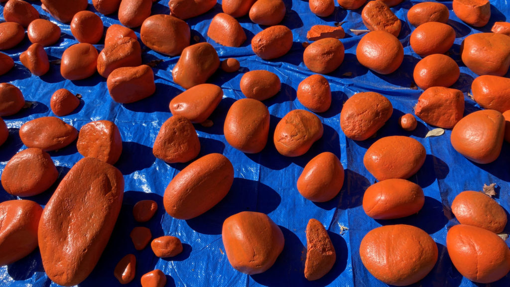 Orange painted rocks, drying in the sun on a big blue tarp