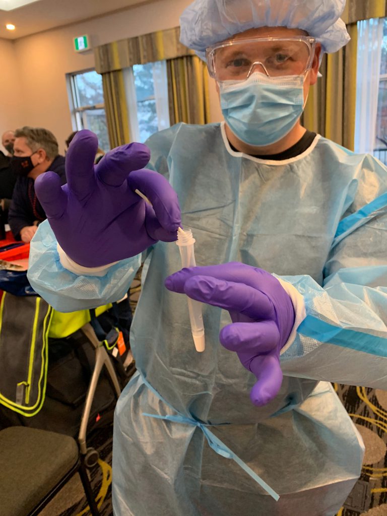 A person dressed in full PPE holds up a COVID-19 swab test.