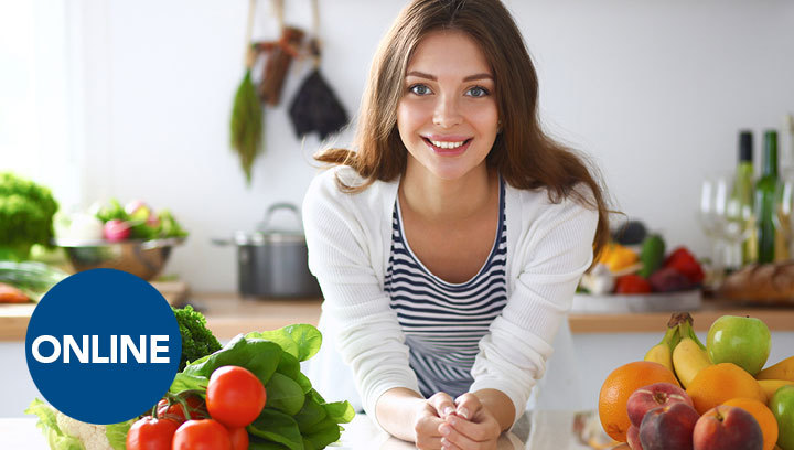 A person in a kitchen setting leaning over a counter with fresh fruit and veggies next to them