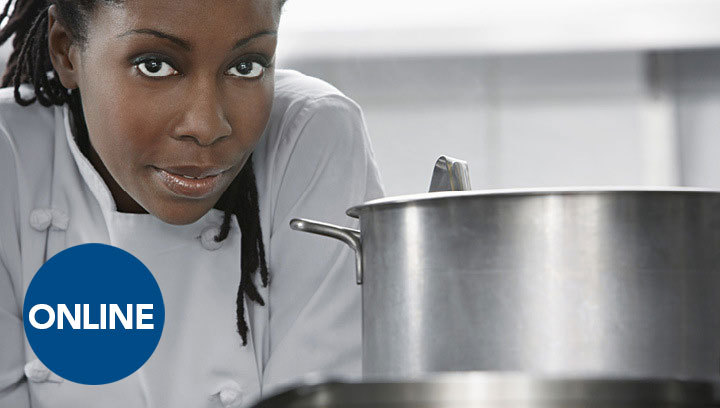 A person in a white chef coat leaning next to a silver pot in a kitchen