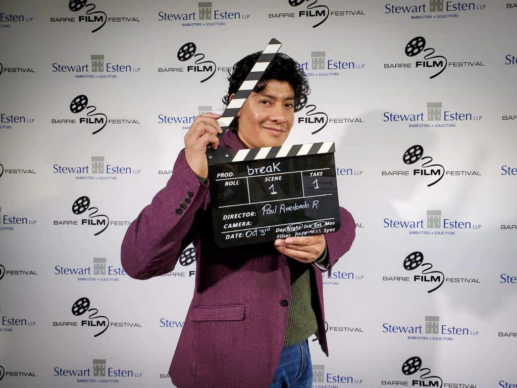 Person smiles at the camera while holding up a clapperboard.