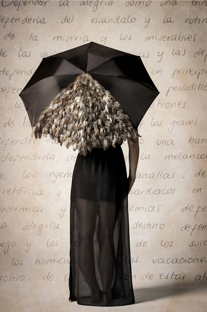 Woman standing facing a wall holding an umbrella with feathers on it with a word display in the background