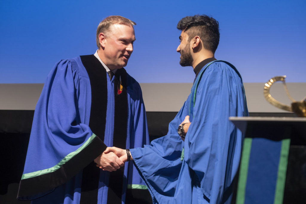 President Kevin Weaver shaking the hand of graduate who is wearing a blue gown.