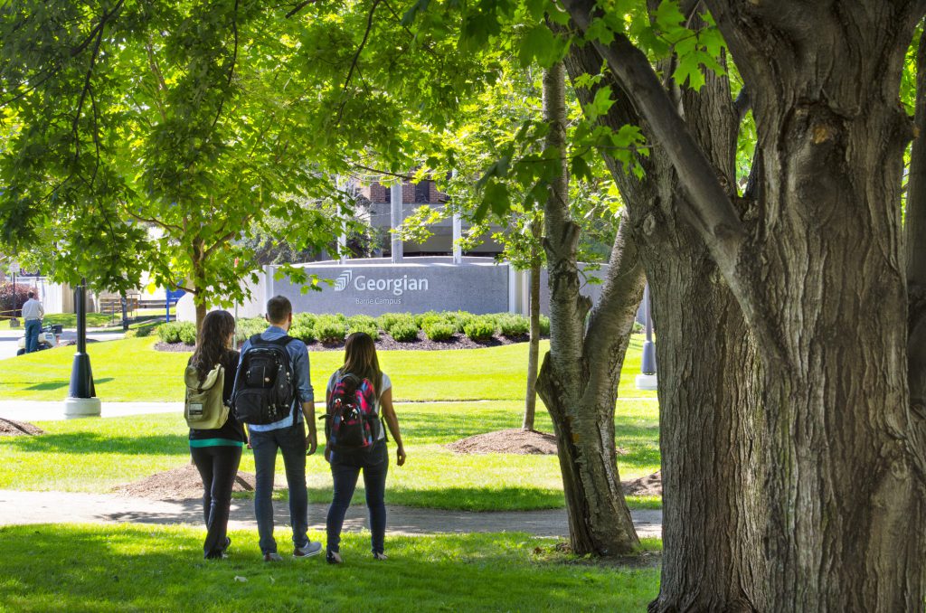 3 students walking with backpacks on in the summer foliage on the Barrie Campus