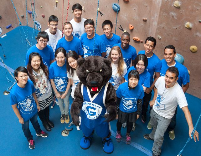 Students and growler standing beside rock climbing wall in fitness centre