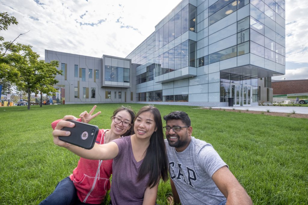 2 female students and 1 male student takes selfie outside N building