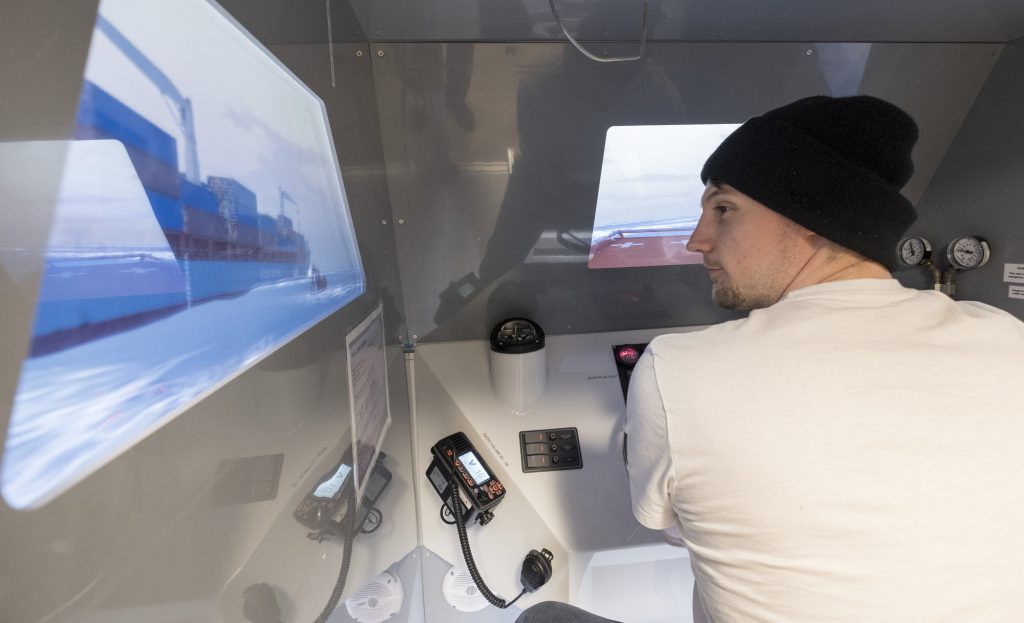 young man wearing a toque and navigating a ship in a marine simulator