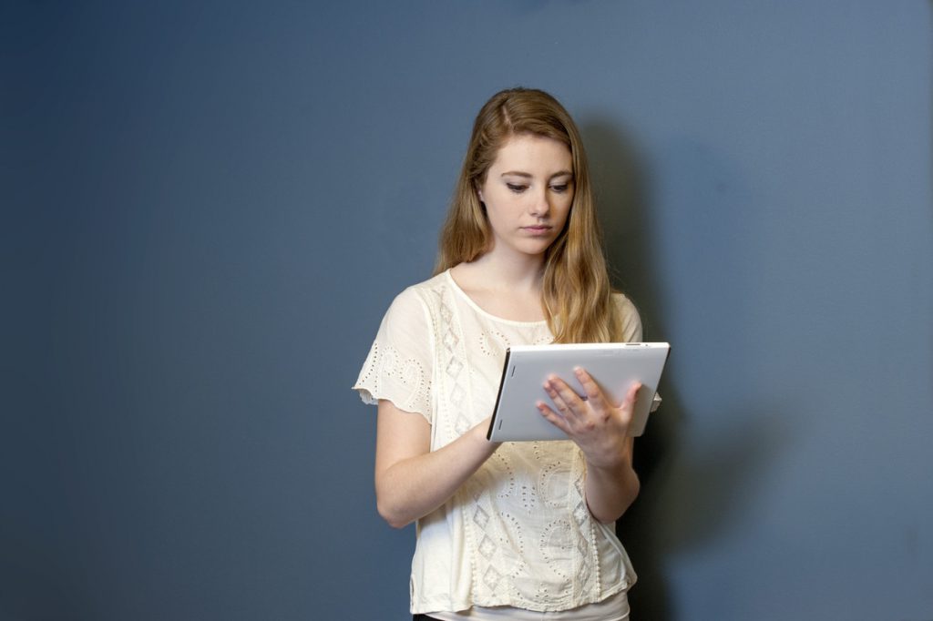 A girl leans against a wall while holding a tablet