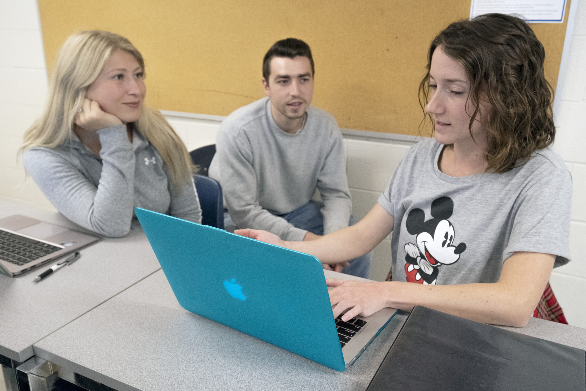 2 female and 1 male student sitting in a classroom working on a laptop