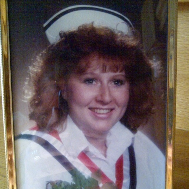 Person dressed in a nurse's uniform smiles at the camera in a framed photo.